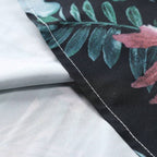 Detalhe da costura da Camisa Vinser Amazônica, destacando o acabamento reforçado sobre a estampa tropical de folhas em tons de verde, azul e rosa sobre fundo preto.