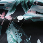 Detalhe do tecido da Camisa Vinser Amazônica, evidenciando a textura, os botões e a estampa tropical de folhas em tons de verde, azul e rosa sobre fundo preto.