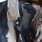 Detalhe da gola da Camisa Vinser Azul Atlântico, destacando o acabamento da gola, o botão frontal e a estampa abstrata inspirada nas ondas do mar em tons de azul, branco, cinza e dourado.