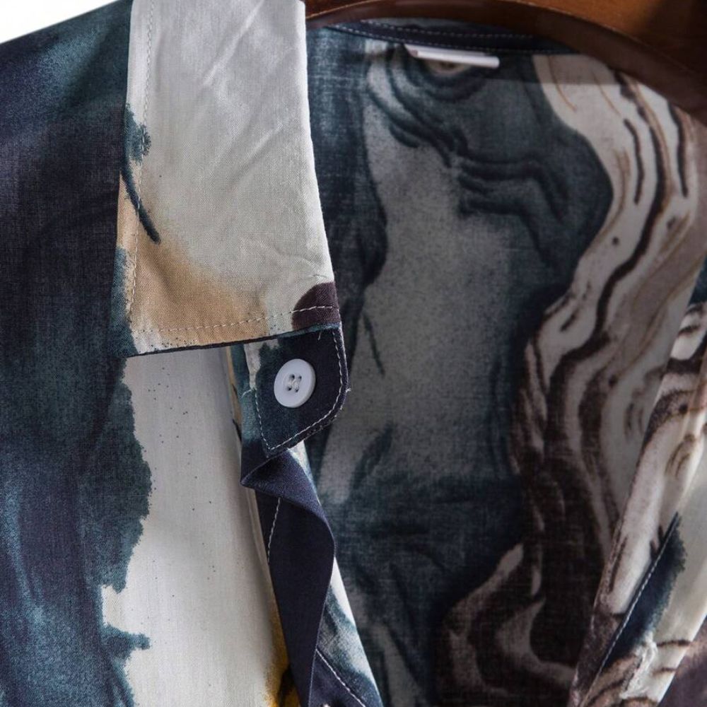 Detalhe da gola da Camisa Vinser Azul Atlântico, destacando o acabamento da gola, o botão frontal e a estampa abstrata inspirada nas ondas do mar em tons de azul, branco, cinza e dourado.