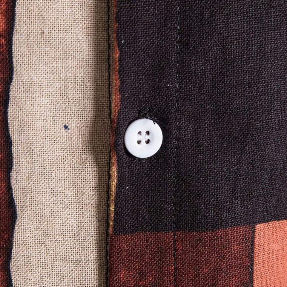 Detalhe do botão e da costura da camisa masculina Vinser Búzios, com tecido estampado em tons de preto, bege, vinho e mostarda.