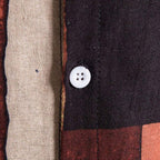 Detalhe do botão e da costura da camisa masculina Vinser Búzios, com tecido estampado em tons de preto, bege, vinho e mostarda.
