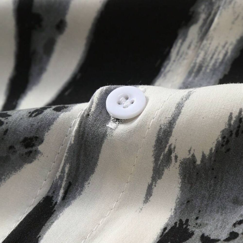 Detalhe do tecido da Camisa Vinser Costa Noturna, destacando a textura, o botão frontal e a estampa abstrata em preto, branco e cinza sobre tecido leve e confortável.