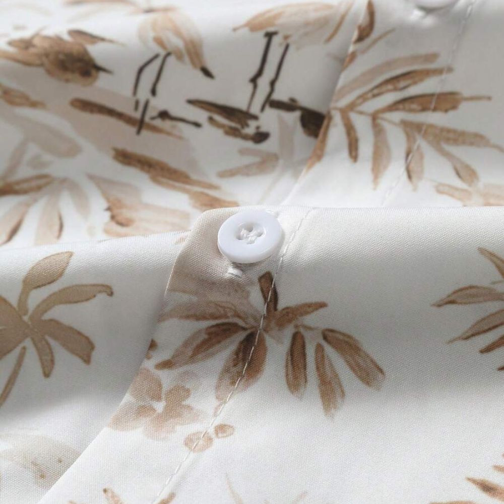 Detalhe do tecido da Camisa Vinser Costa, destacando a textura leve, o acabamento de qualidade, o botão frontal e a estampa tropical em tons de branco e bege.