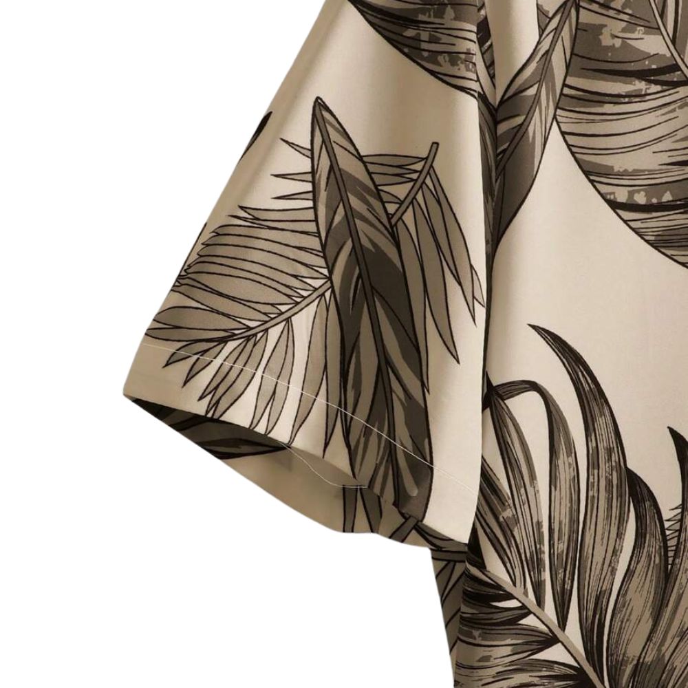 Detalhe da manga da Camisa Vinser Duna Atlântica, com estampa tropical de folhas em tons de marrom sobre fundo bege, evidenciando o acabamento da costura e a leveza do tecido.