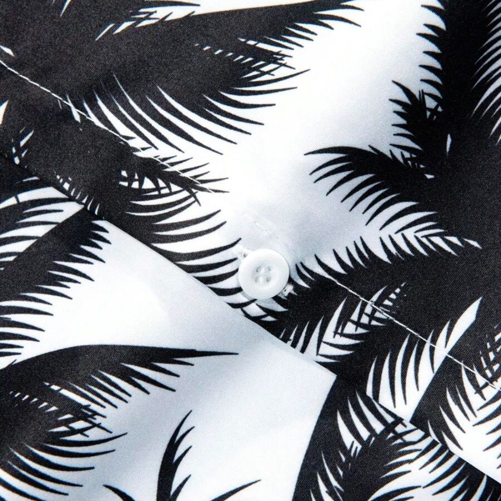 Detalhe do tecido da camisa masculina Vinser Espelho com estampa de coqueiros pretos, botão branco, acabamento premium e costuras refinadas