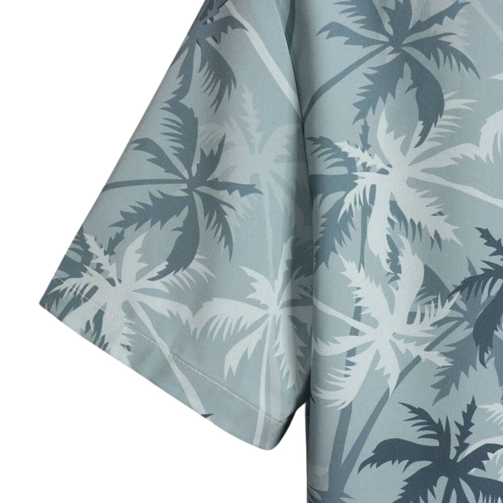 Close da manga da Camisa Vinser Horizonte Azul, destacando a estampa tropical de coqueiros em tons de azul e cinza, o tecido leve, a manga curta e o acabamento premium da peça