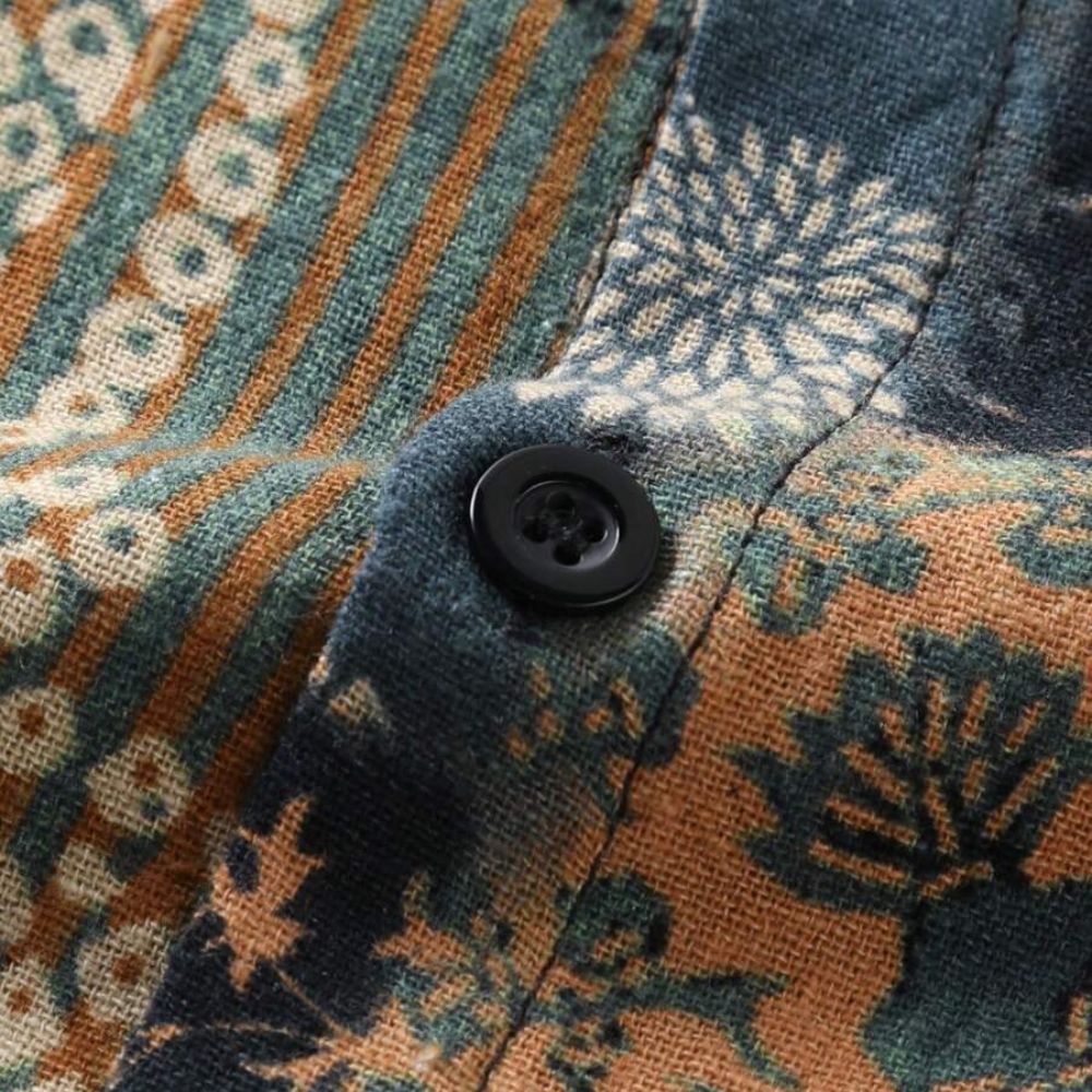 Detalhe da Camisa Vinser Mosaico destacando o botão preto, as costuras reforçadas e a estampa patchwork em tons de verde-musgo, bege, marrom e preto, evidenciando a textura do tecido e o acabamento refinado.
