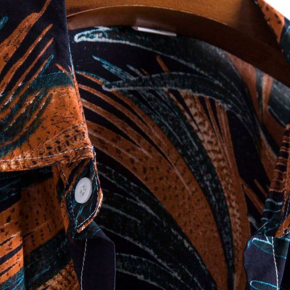 Detalhe da gola da Camisa Vinser Noronha, destacando o acabamento refinado, o tecido leve e a estampa tropical de folhas em tons de laranja e azul-petróleo sobre fundo azul-marinho.