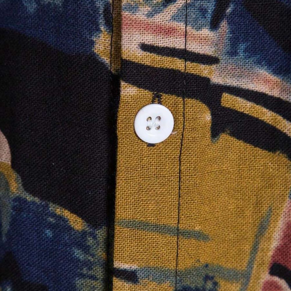 Detalhe do botão e da costura da camisa masculina Vinser Paraty, com tecido estampado em azul-marinho e mostarda.
