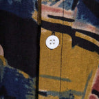 Detalhe do botão e da costura da camisa masculina Vinser Paraty, com tecido estampado em azul-marinho e mostarda.