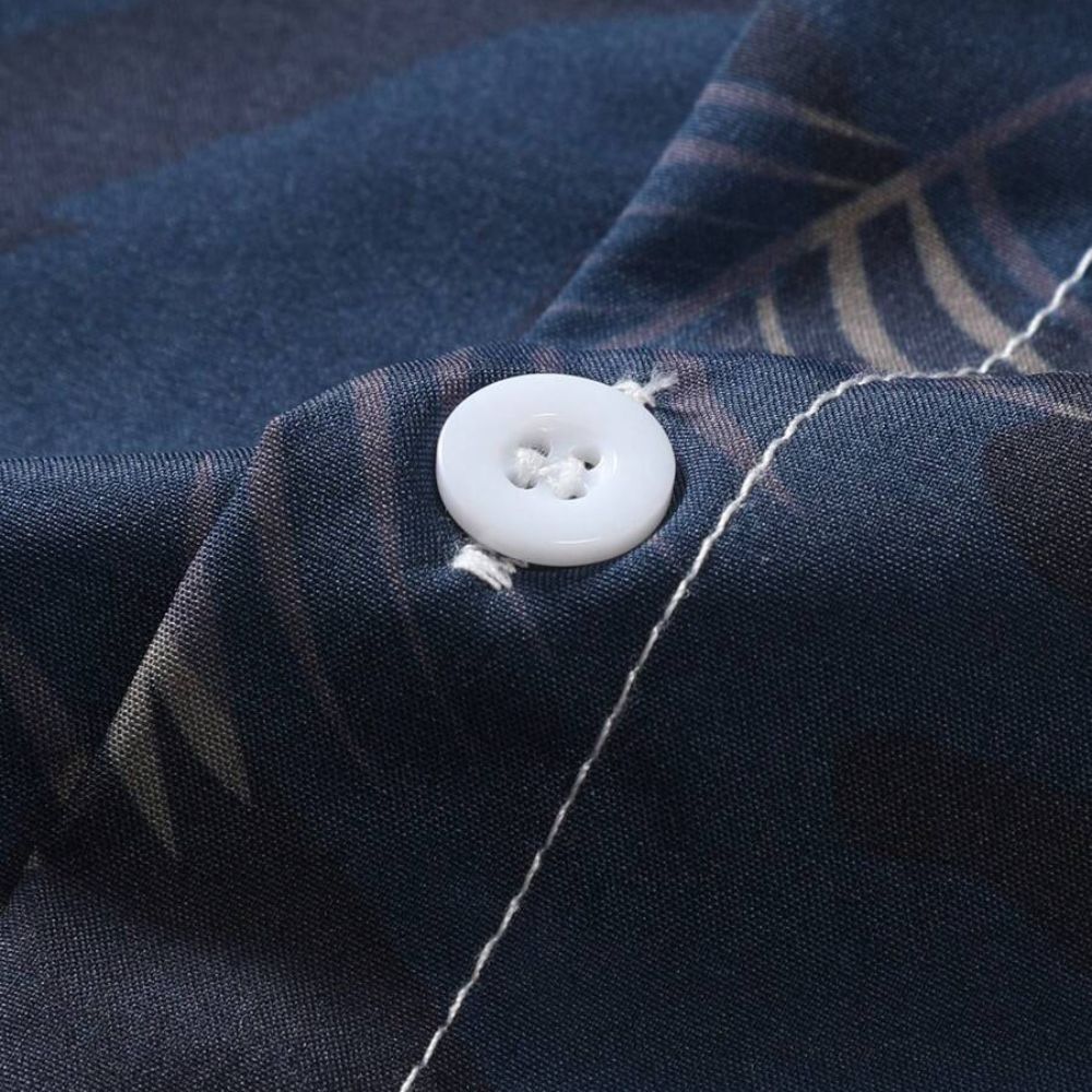 Close do botão e do tecido da camisa masculina Vinser Porto de Galinhas, destacando a textura do tecido, a estampa de folhas e o acabamento premium.