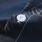 Close do botão e do tecido da camisa masculina Vinser Porto de Galinhas, destacando a textura do tecido, a estampa de folhas e o acabamento premium.