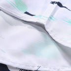 Detalhe do acabamento e da costura da camisa masculina Vinser Praia do Forte com estampa tropical de coqueiros em preto e verde-água sobre fundo branco. Tecido leve, respirável, com costuras reforçadas e acabamento premium.