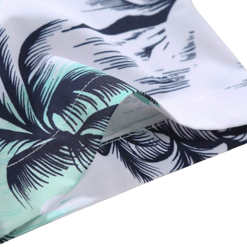 Detalhe da manga da camisa masculina Vinser Praia do Forte com estampa tropical de coqueiros em preto e verde-água sobre fundo branco. Acabamento premium, costura reforçada e tecido leve, macio e respirável.